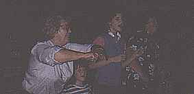 <Family standing in living room making motions with hands as part of some game.>